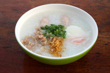 Side view Rice porridge or Minced Pork Congee with Soft Boiled Egg in bowl on wood brown table - favorite Breakfast in Asia - Morning food 