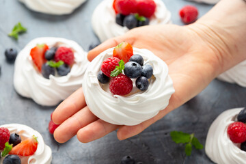 Woman's Hand hold meringue nest mini pavlova cake with fresh berries strawberry blueberry raspberry and mint for healthy desert