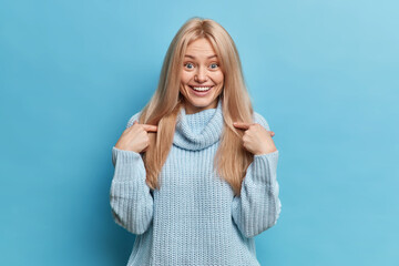 Portrait of surprised blonde Caucasian woman has happy expression points at herself cannot believe...
