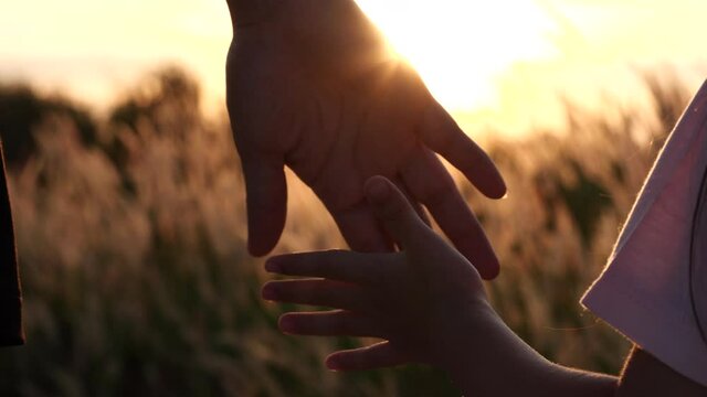 Close-up of mother and daughter hands joining together with sunset sunlight flare in natural background, Slow motion. Beautiful romantic moment between mother and litle child. Happy Family and Relatio