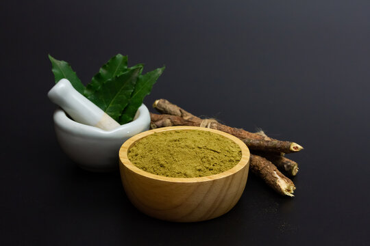 neem powder in wooden bowl and neem leaf in white mortar and pestle on black background.