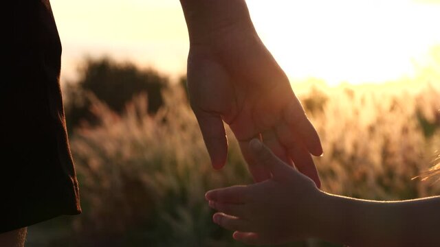 Close-up of mother and daughter hands joining together with sunset sunlight flare in natural background, Slow motion. Beautiful romantic moment between mother and litle child. Happy Family and Relatio