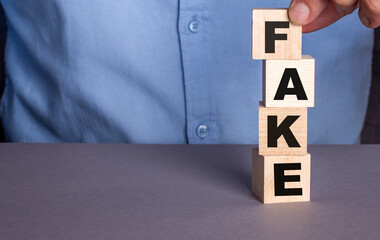 A man in a blue shirt composes the word FAKE from wooden cubes vertically