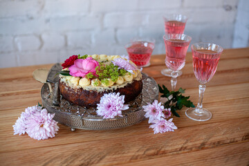 festive cake and rose wine in glasses, flowers on wooden table for birthday