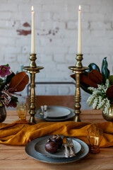 long wooden party table with stylish decoration, with candlesticks, vases of flowers, plates and food in a room with a white brick wall