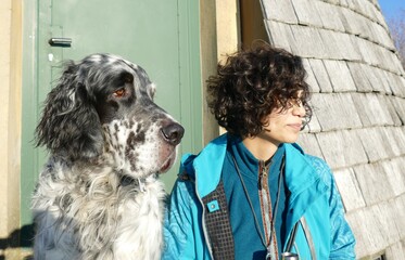 English Setter dog and young woman with wild dark hair both looking sideways into the same...