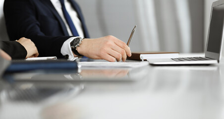 Unknown businessmen and woman sitting, using laptop computer and discussing questions at meeting in modern office, close-up
