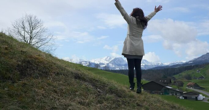 Woman Enjoys Fresh Air and Watching at Scenic Mountains. Tourist Travel in Picturesque Swiss Alps. Green Grass Pastures Meadows. Cottages in Village. Switzerland Europe