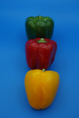 Three paprika peppers: yellow, red and green against a blue background close-up.