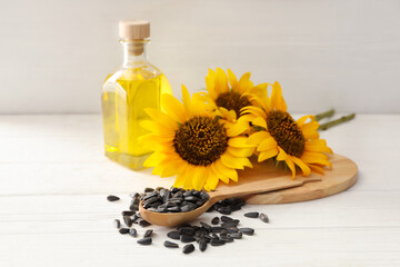 Sunflowers, bottle of oil and seeds on white wooden table