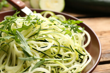 Tasty zucchini pasta with arugula on wooden table, closeup