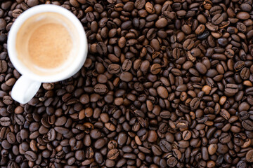 Flat lay with copy space, (selective focus) A defocused white espresso cup with some creamy coffee is placed on some roasted coffee beans.