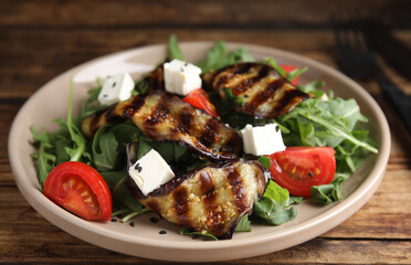 Delicious salad with roasted eggplant, feta cheese and arugula served on wooden table, closeup