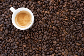 Flat lay with copy space, (selective focus) A white espresso cup with some creamy coffee is placed on some blurred roasted coffee beans.