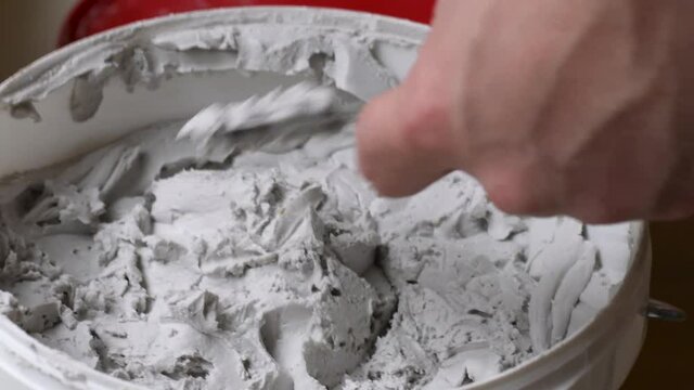 Using a putty knife to get some spackle compound from the bucket as it is time for spackling the holes in the wall in a room, before painting.