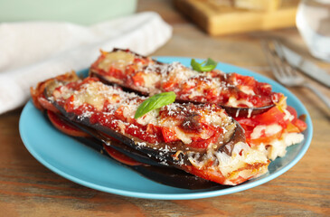 Baked eggplant with tomatoes, cheese and basil on wooden table, closeup