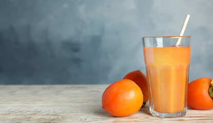 Tasty persimmon smoothie and fresh fruits on white wooden table against light blue background. Space for text