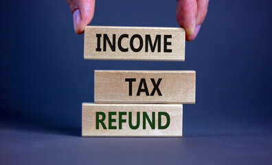 Income tax refund symbol. Wooden blocks form the words 'Income tax refund' on grey background. Male...