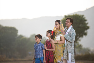 Happy rural Indian family looking away at agricultural field