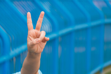 Woman hand showing peace gesture or victory sign with blurred blue fence background