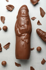 Flat lay composition with whole and broken chocolate Santa Claus candies on light grey table
