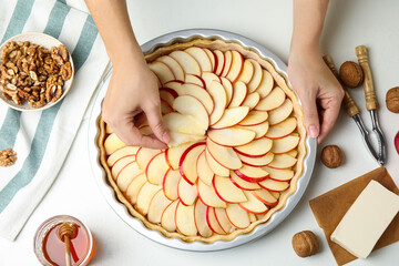 Woman putting apple slice into baking dish with dough to make traditional English pie at white...
