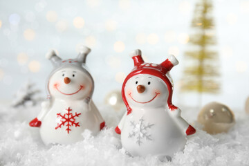Christmas composition with decorative snowmen on artificial snow against blurred festive lights