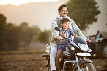 Happy rural Indian farmer with son riding on motorcycle