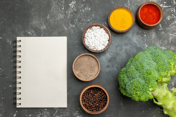 Obraz na płótnie Canvas Overhead view of healthy meal with brocoli and carrots on a black plate and spices with notebook