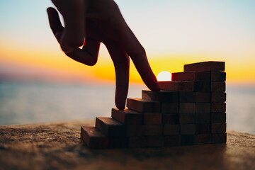 finger like a person stepping up wood block stacking as step stair and sun background. Business success, win concept.