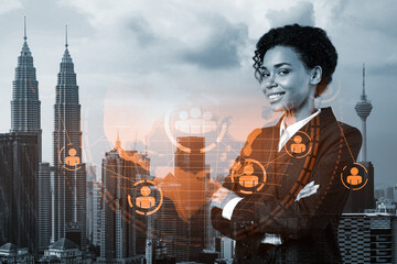 Fototapeta premium Smiling black woman HR director at international company is thinking about recruitment of highly qualified specialists. Women in business concept. Social media hologram icons over Kuala Lumpur.