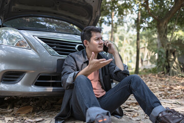 Man usea cellphone call garage in front of the open hood of a broken car on the road in the forest. Car breakdown concept.