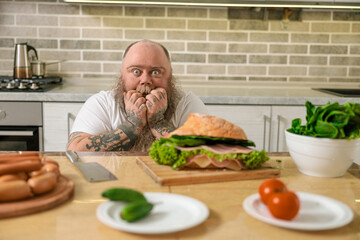 Emotional fat funny and tattooed man with food at the kitchen at home