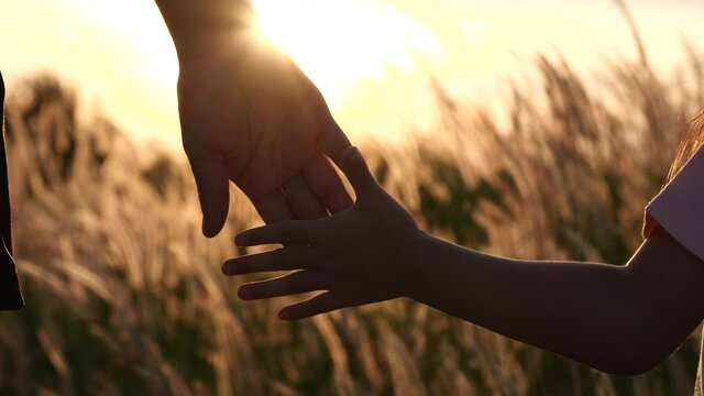 Close-up of mother and daughter hands joining together with sunset sunlight flare in natural background, Slow motion. Beautiful romantic moment between mother and litle child. Happy Family Concept
