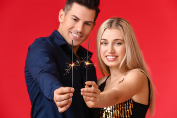 Happy young couple with Christmas sparklers on color background