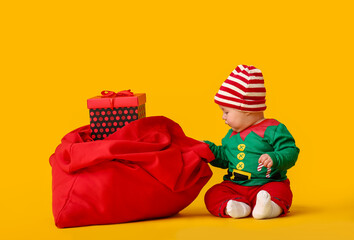 Cute little baby in elf's costume and with Santa bag on color background