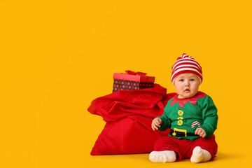 Cute little baby in elf's costume and with Santa bag on color background