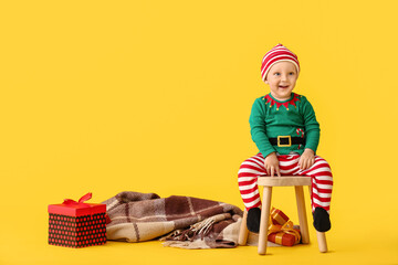 Cute little baby in elf's costume and with gifts on color background