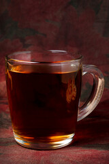 glass transparent mug with black tea on dark red background