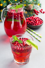 Homemade lingonberry and lime punch or limeade in a glass and pitcher, christmas tree decoration with bokeh, vertical
