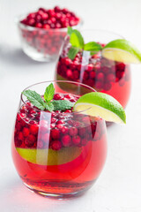 Homemade lingonberry and lime punch or limeade in glass and pitcher on gray background, vertical