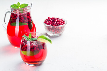 Lingonberry and lime punch or limeade in glass and pitcher on gray background, horizontal, copy space