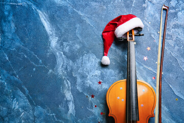 Violin with Santa Claus hat on color background