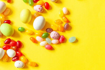 Happy Easter concept. Preparation for holiday. Easter candy chocolate eggs and jellybean sweets isolated on trendy yellow background. Simple minimalism flat lay top view copy space.