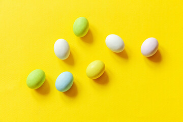 Happy Easter concept. Preparation for holiday. Easter candy chocolate eggs colorful pastel sweets and bunny toy isolated on trendy yellow background. Simple minimalism flat lay top view copy space.