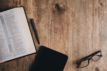 Open Bible and notebook on a wooden desk. Top view flat lay.