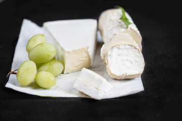 White goat cheese wih green grape on a  black background. Fresh goat cheese with copy space, cut in pieces