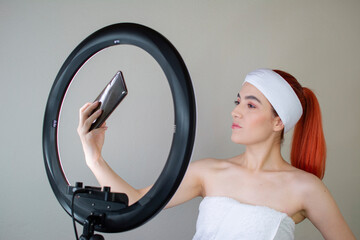 A beautiful woman taking a selfie with her smartphone in front of the ring of light after applying makeup
