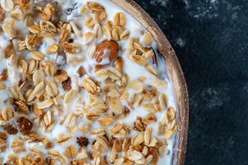 Granola with oatmeal, dried fruit, honey, raisins, dry cranberry, almond and cashew nuts with yogurt in a coconut bowl, close up