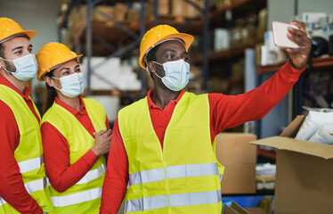 Multiracial people taking a selfie at work in warehouse while wearing surgical face masks for...